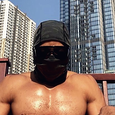 Portrait of the author wearing a dark head covering and sunglasses, with high-rise buildings behind.